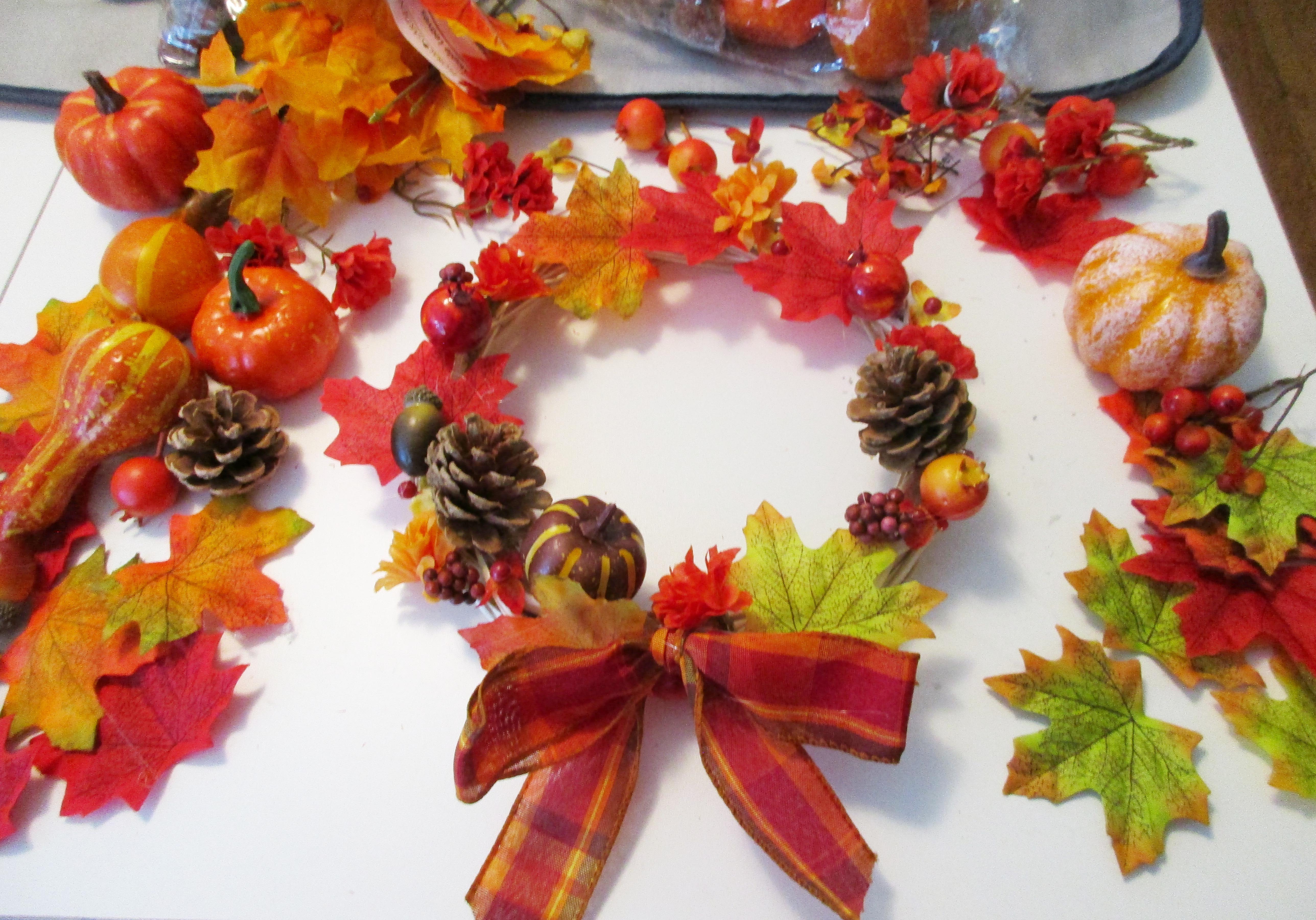 fall wreath surrounded by leaves, gourds, berries, and pine cones