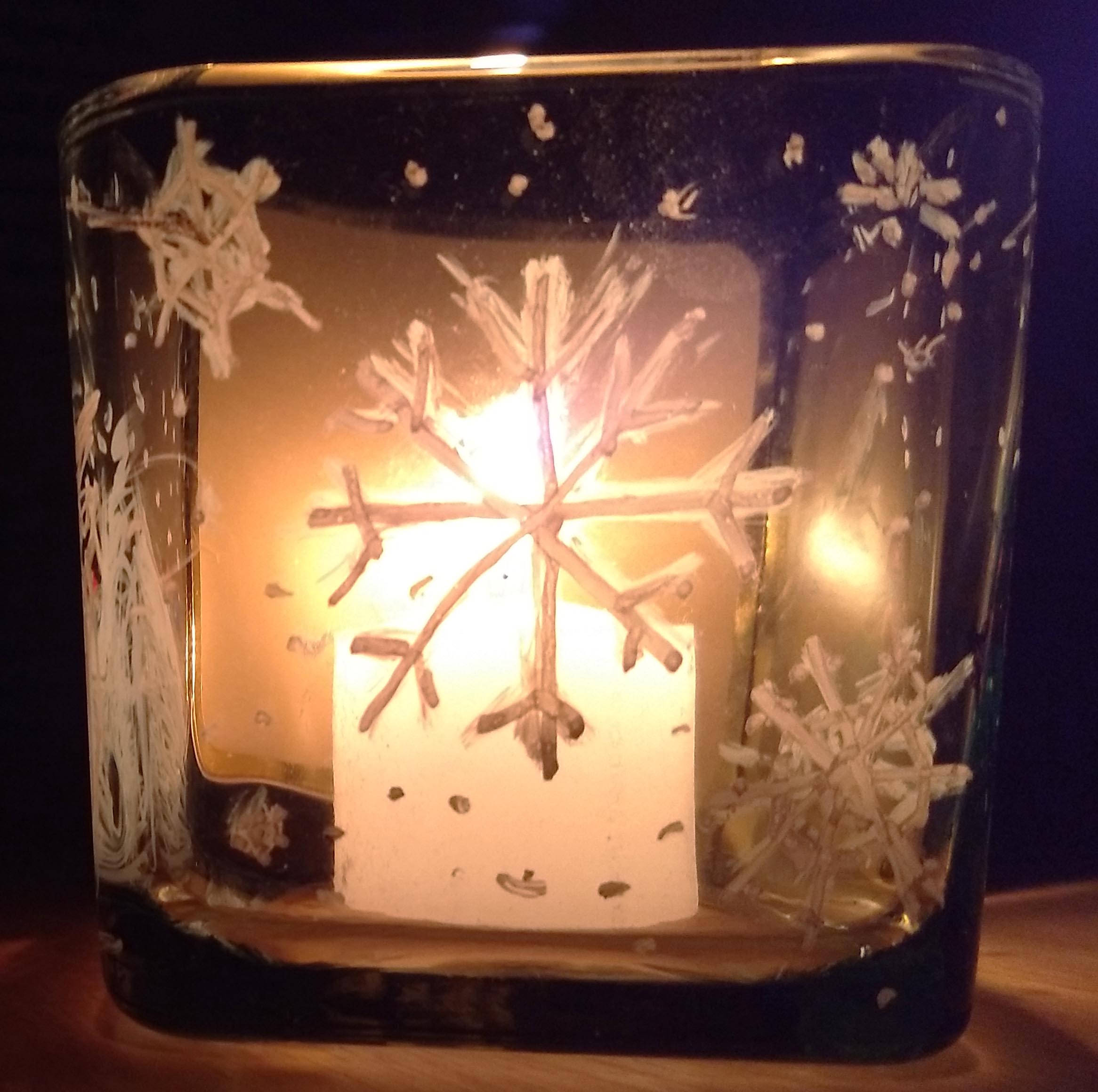 candle shining through glass holder painted with snowflakes
