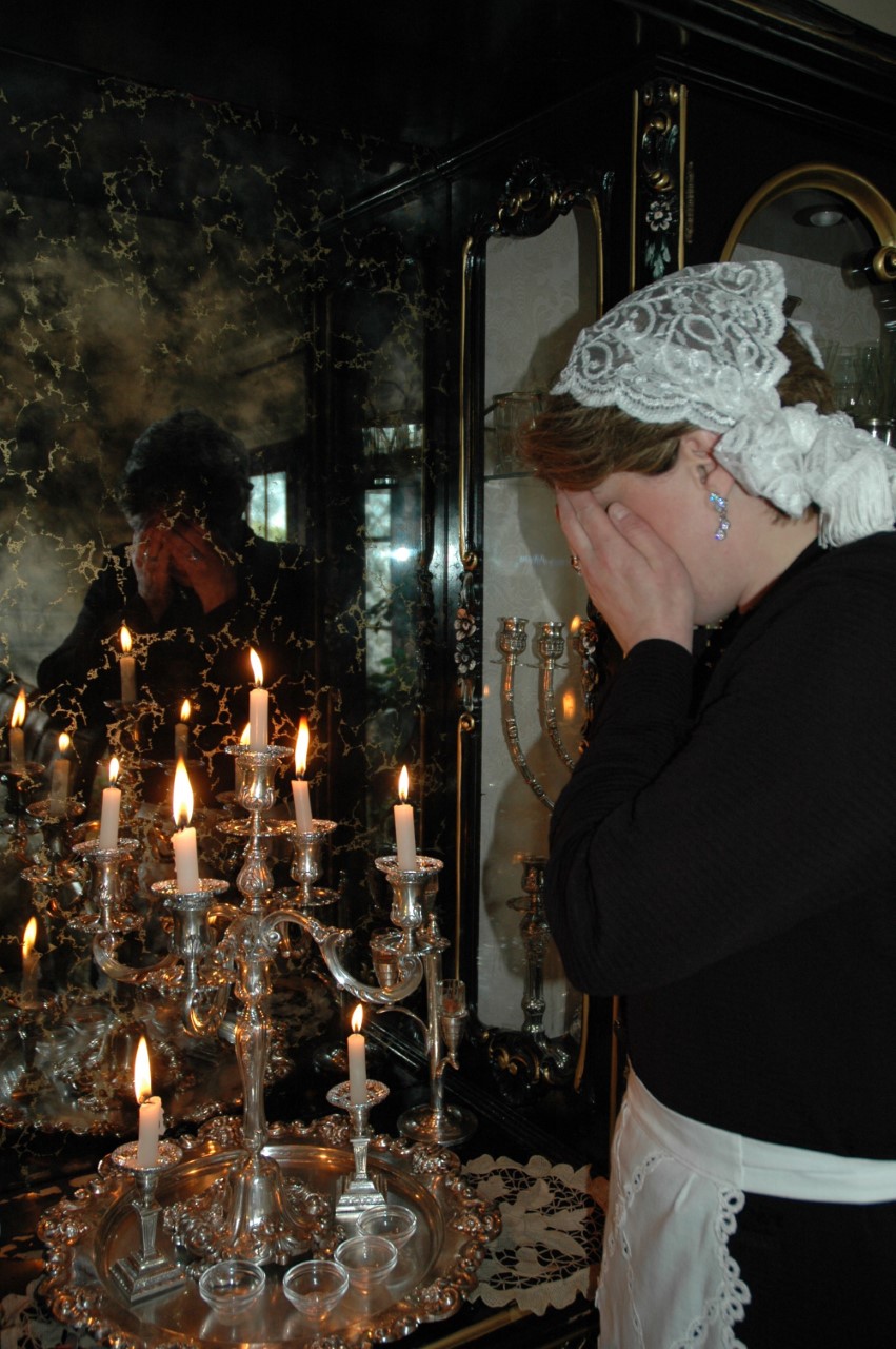 Woman dressed in black with white lace head covering stands in front of lit candles