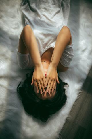 woman lying on bed covering her eyes 