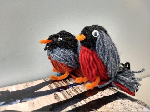 two robins made of yarn. black head and back, gray wings, red fronts