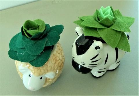 two felt succulents in shades of green, in ceramic planters shaped like a lamb and a zebra