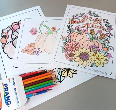 colored pencils on top of several coloring pages on fall themes