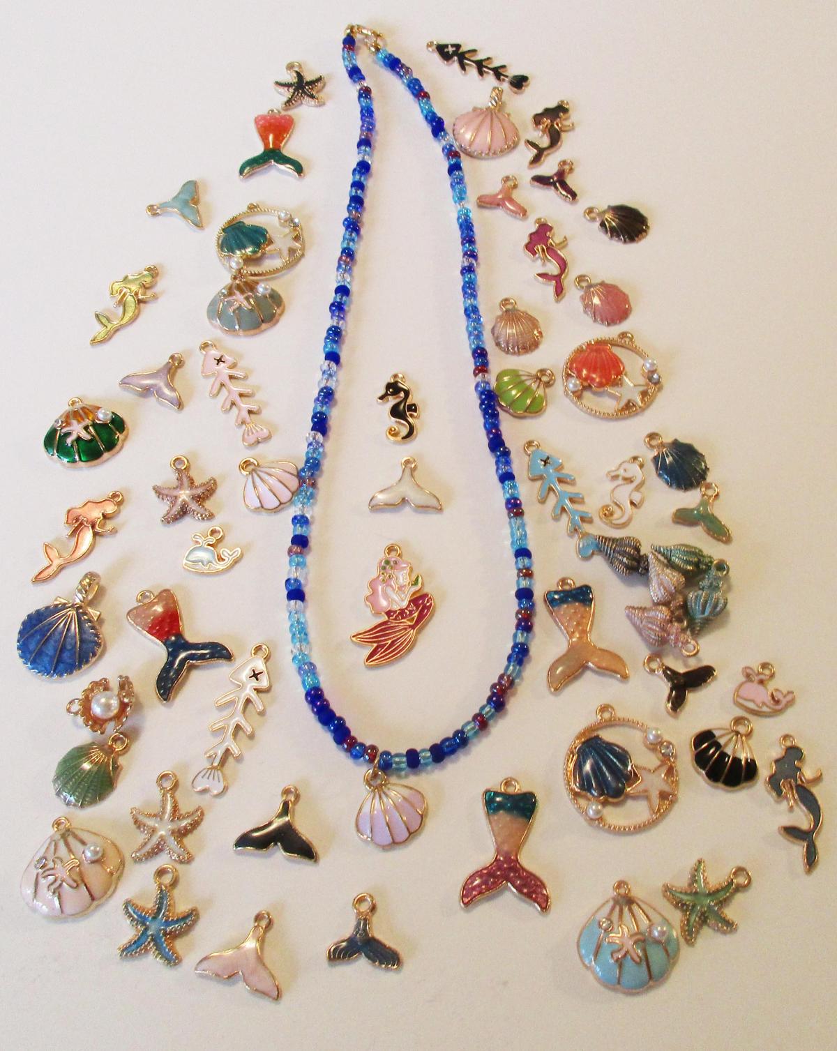 blue beaded necklace with pink shell charm, surrounded by other enamel charms in ocean themes