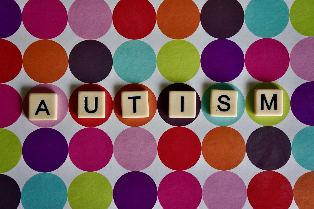 AUTISM SPELLED OUT WITH SCRABLLE TILES WITH RAINBOW BACKGROUND