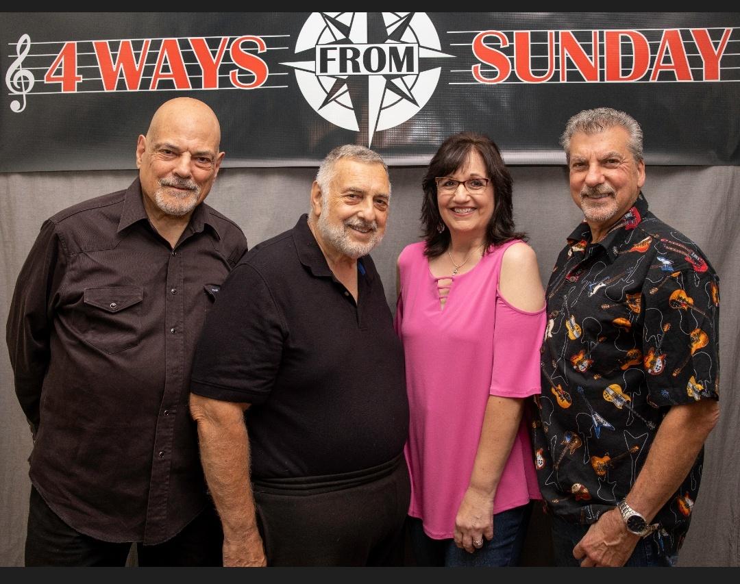 Members of 4 Ways From Sunday smiling in front of their banner